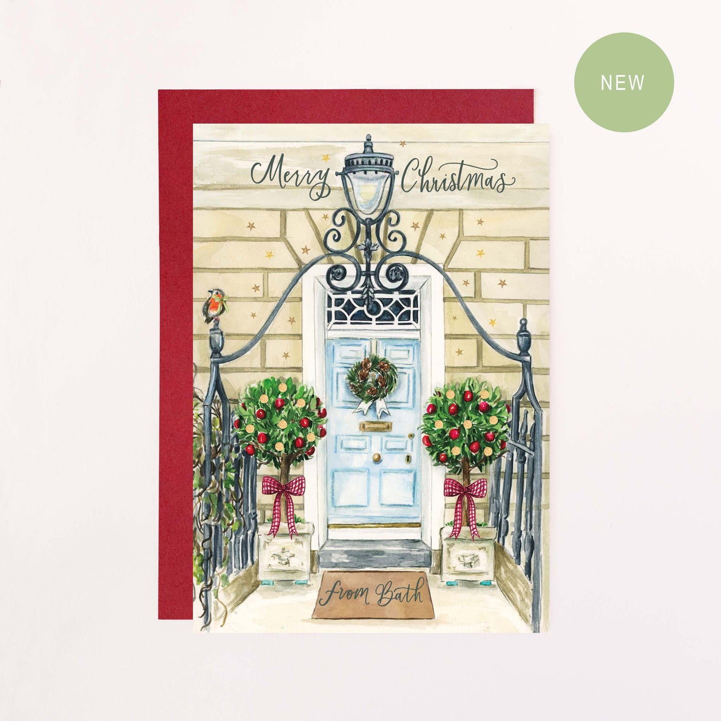 A festive greeting card with green calligraphy text reading 'Merry Christmas From Bath ' with a drawing of A Bath Georgian town house decorated with bows, Baubles, faux glitter stars and a red robin