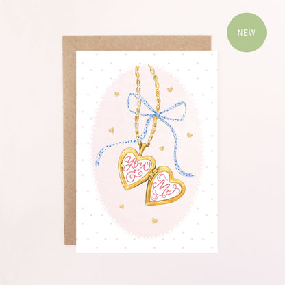 Greeting card with heart-shaped locket and 'You & Me' text on a pink background
