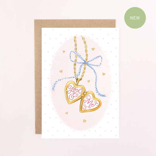 Greeting card with heart-shaped locket and 'You & Me' text on a pink background