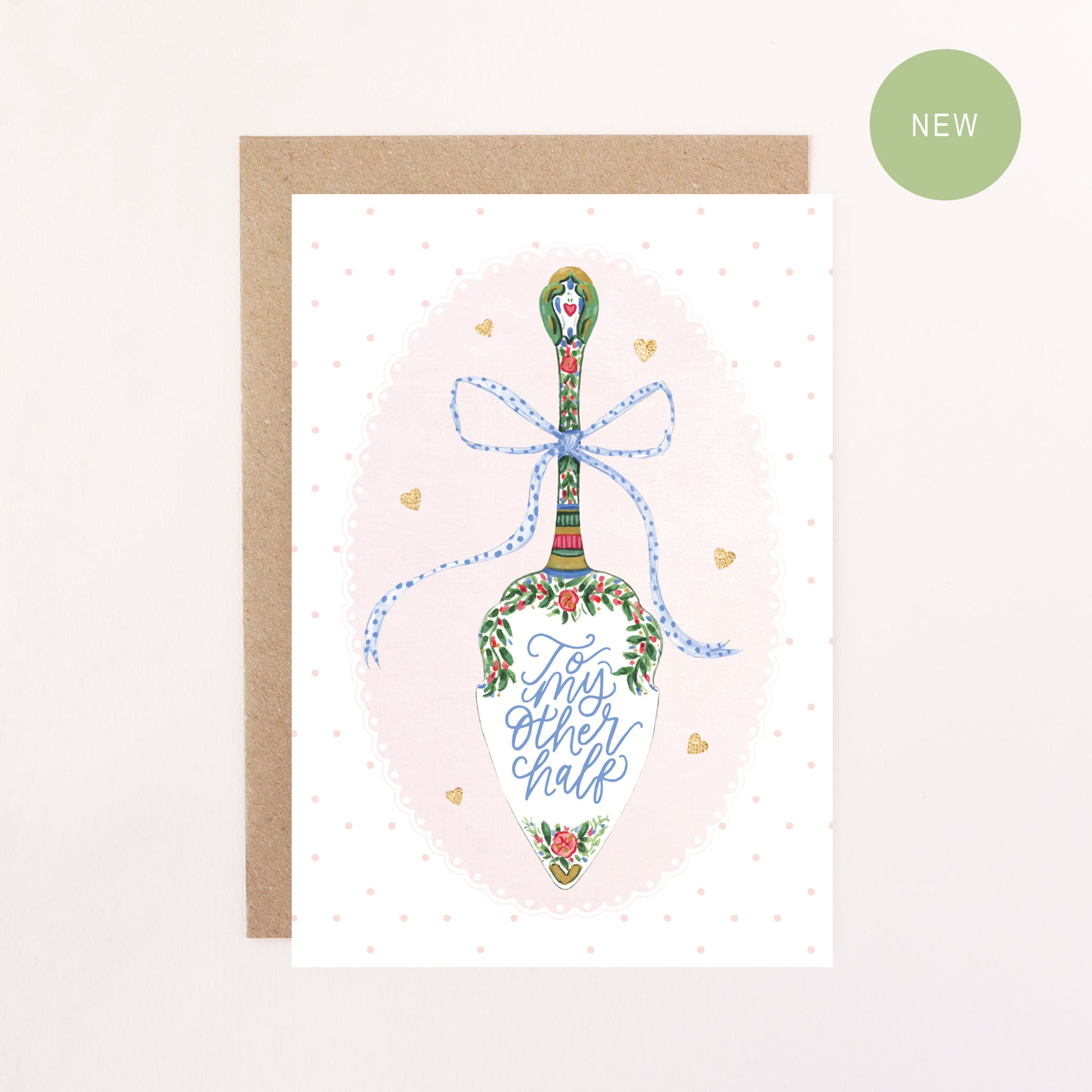 Greeting card with a decorative cake slice, blue bow, faux glitter hearts, polka dots and a doily illustration and text reading' To my other half' on a light pink background.