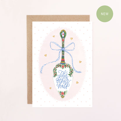 Greeting card with a decorative cake slice, blue bow, faux glitter hearts, polka dots and a doily illustration and text reading' To my other half' on a light pink background.