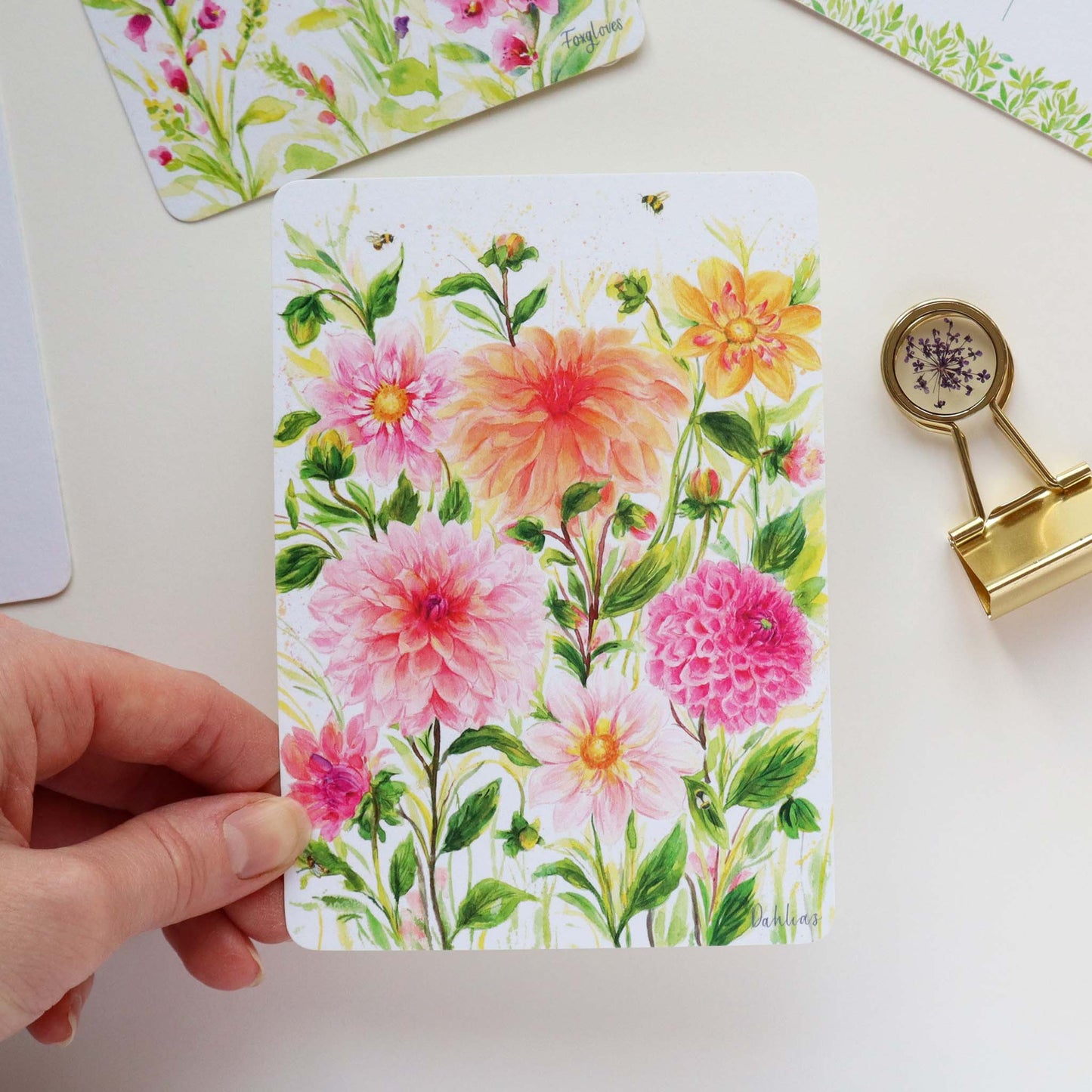 Floral Postcard with Dahlias held by a hand and additional postcards in the background.
